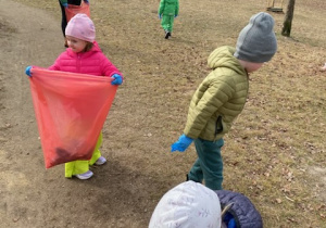 Zdjęcie przedstawia dzieci porządkujące teren parku w pobliżu przedszkola.