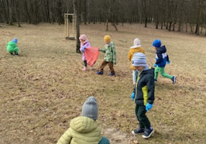 Zdjęcie przedstawia dzieci porządkujące teren parku w pobliżu przedszkola.