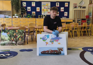 Zdjęcie przedstawia prowadzącego warsztaty, który opowiada dzieciom jak powstaje czekolada.