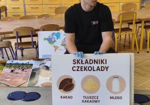 Zdjęcie przedstawia prowadzącego warsztaty,który opowiada dzieciom jak powstaje czekolada i z jakich składników się składa.
