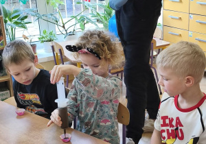 Na tym zdjęciu widać prowadzącego oraz troje dzieci, które napełniają foremki płynną czekoladą.