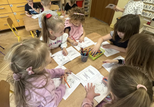 Na tym zdjęciu widać dzieci siedzące przy stolikach i wykonujące karty pracy.