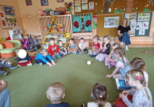 Na tym zdjęciu widać dzieci siedzące w kole na dywanie podczas zabawy słownej z wykorzystaniem piłeczki.