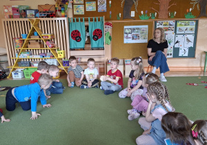 Na tym zdjęciu widać dzieci siedzące w kole na dywanie podczas zabawy słownej z wykorzystaniem piłeczki.