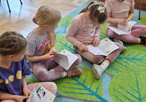 Zdjęcie przedstawia cztery dziewczynki siedzące na dywanie z kartami pracy, które otrzymały na warsztatach.