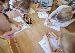Na tym zdjęciu widać kilkoro dzieci, które wykonują zadanie w książeczce z kartami pracy.