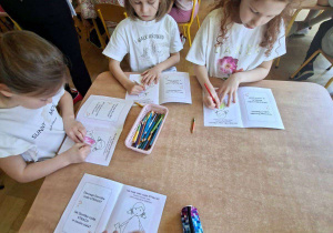 Na tym zdjęciu widać kilkoro dzieci, które wykonują zadanie w książeczce z kartami pracy.