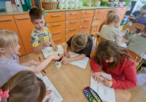 Na tym zdjęciu widać kilkoro dzieci, które wykonują zadanie w książeczce z kartami pracy.