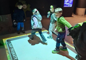 Zdjęcie przedstawia kilkoro dzieci bawiących się na dywanie interaktywnym.