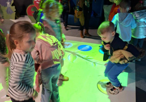 Zdjęcie przedstawia dzieci z grupy III podczas zabaw na dywanie interaktywnym.