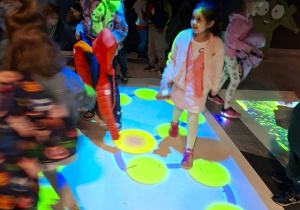 Na tym zdjeciu widać kilkoro dzieci bawiących się na dywanie interaktywnym.