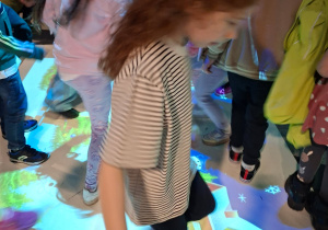 Na tym zdjęciu widać Mayę z grupy IV oraz inne dzieci bawiące się na dywanie interaktywnym.