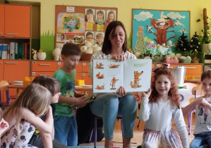 Zdjęcie przedstawia mamę Kuby pokazująca ilustracje w książeczce oraz kilkoro dzieci.