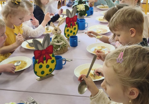 Zdjęcie przedstawia dzieci przy świątecznym stole, spożywające żurek z jajkiem.