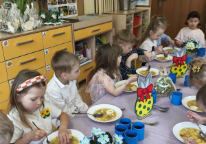 Zdjęcie przedstawia dzieci przy świątecznym stole, spożywające żurek z jajkiem.