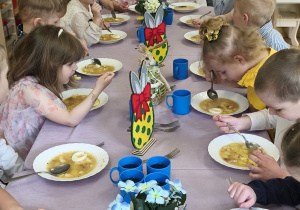 Zdjęcie przedstawia dzieci przy świątecznym stole, spożywające żurek z jajkiem.