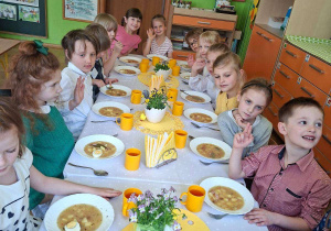 Zdjęcie przedstawia dzieci siedzące przy świątecznym stole, spożywające żurek z jajkiem.