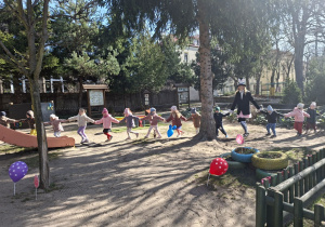 W tle zdjęcia widać korowód dzieci podążający za zajączkiem wielkanocnym.