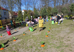 Zdjęcie przedstawia dzieci skaczące w workach między marchewkami.