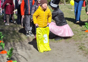 Zdjęcie przedstawia dzieci skaczące w workach między marchewkami.