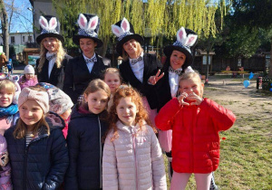 Na tym zdjęciu widać kilka dziewczynek wraz z prowadzącymi w strojach króliczków w ogrodzie przedszkolnym.