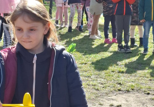 Zdjęcie przedstawia Zuzię M. przenoszącą jajko na łyżce oraz pozostałe dzieci stojące z tyłu.