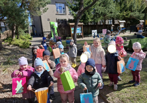 Zdjęcie przedstawia dzieci z prezentami od zajączka odnalezionymi w ogrodzie.