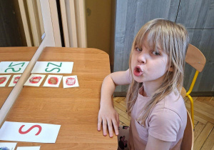 Zdjęcie przedstawia Wandę z grupy IV wykonującą ćwiczenia narządów mowy z wykorzystaniem kart obrazkowych.