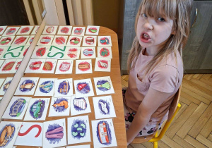 Zdjęcie przedstawia Wandę z grupy IV wykonującą ćwiczenia narządów mowy z wykorzystaniem kart obrazkowych.