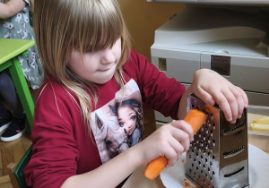 Zdjęcie przedstawia Wandę z grupy IV ścierającą na tarce marchewkę.