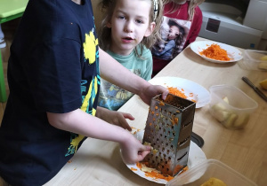 Zdjęcie przedstawia Stasia W. z grupy IV ścierającego na tarce marchewkę.