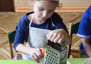 Zdjęcie przedstawia Oliwię z grupy III ścierającą na tarce marchewkę.