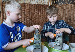 Zdjęcie przedstawia Adama W. i Adama M. z grupy III ścierających na tarce marchewkę.