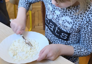 Na tym zdjęciu widać jedną z dziewczynek rozdrabniającą widelcem twarożek.