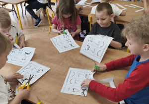 Zdjęcie przedstawia kilkoro dzieci z grupy III, które wycinaja elementy do wykonania karty pracy.