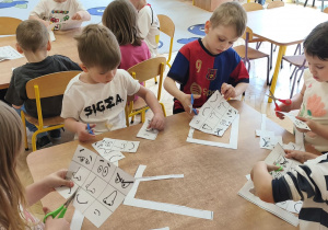 Zdjęcie przedstawia kilkoro dzieci z grupy III i IV, które wycinaja elementy do wykonania karty pracy.
