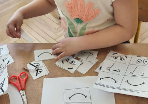 Zdjęcie przedstawia jedną z dziewczynek uczestniczącą w zajęciach, która wycinaja elemnty do wykonania karty pracy.