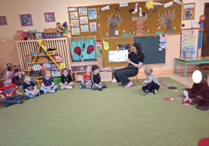 Zdjęcie przedstawia mamę Mikołaja czytającą książeczkę oraz dzieci siedzące w kole, słuchające opowieści.