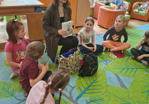 Na tym zdjęciu widać kilkoro dzieci siedzących na dywanie oraz prowadzącą warsztaty.