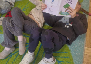 Na tym zdjęciu widać troje dzieci leżących na dywanie podczas słuchania opowiadania.