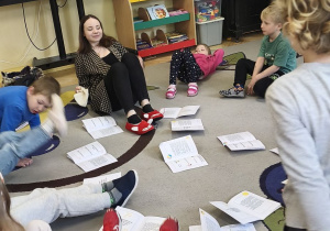 Zdjęcie przedstawia dzieci siedzące na dywanie wraz z prowadzącą zajęcia podczas omawiania tematu.