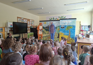 Zdjęcie przedstawia jedną ze scen teatrzyku i dzieci oglądające przedstawienie.