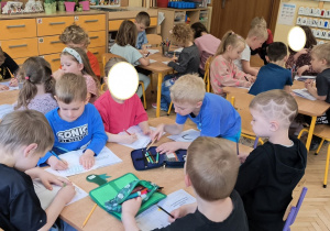 Na tym zdjęciu widać dzieci siedzące przy stolikach, wykonujące kartę pracy dotyczacą smutku.