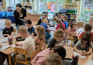 Na tym zdjęciu widać dzieci siedzące przy stolikach, wykonujące kartę pracy dotyczacą smutku.