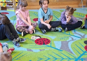 Na tym zdjęciu widać Alę W., Tymka i Zuzię M. siedzących na dywanie podczas zajęć.