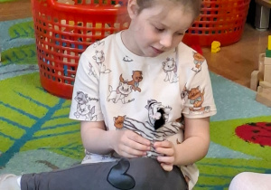 Zdjęcie przedstawia Basię, która siedzi na dywanie podczas zajęć.