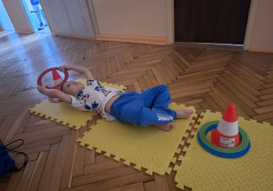 Zdjęcie przedstawia Maksa Z. z grupy II przekładająceo krążki z pachołka na pachołek w lężeniu tyłem.