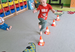 Zdjęcie przedstawia Kubę S. z grupy II wykonującego slalom na jednej nodze między pachołkami.