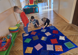 Zdjęcie przedstawia chłopców z grupy III podczas ćwiczeń integracji sensorycznej z wykorzystaniem dywanu sensorycznego.
