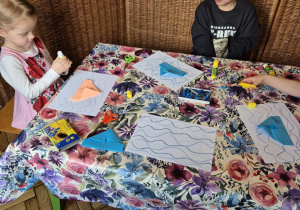 Na tym zdjęciu widać dziewczynkę i chłopca wykonujących żaglówkę metodą origami.